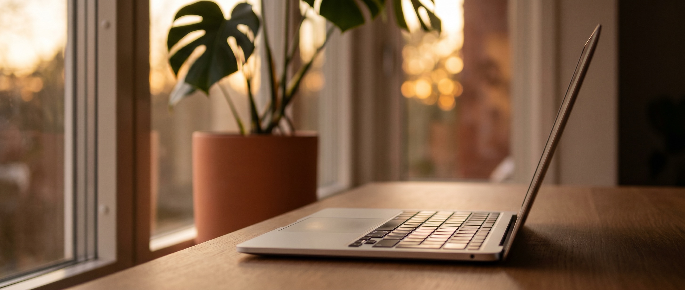 Escritorio cálido con laptop, taza de café, planta y luz dorada